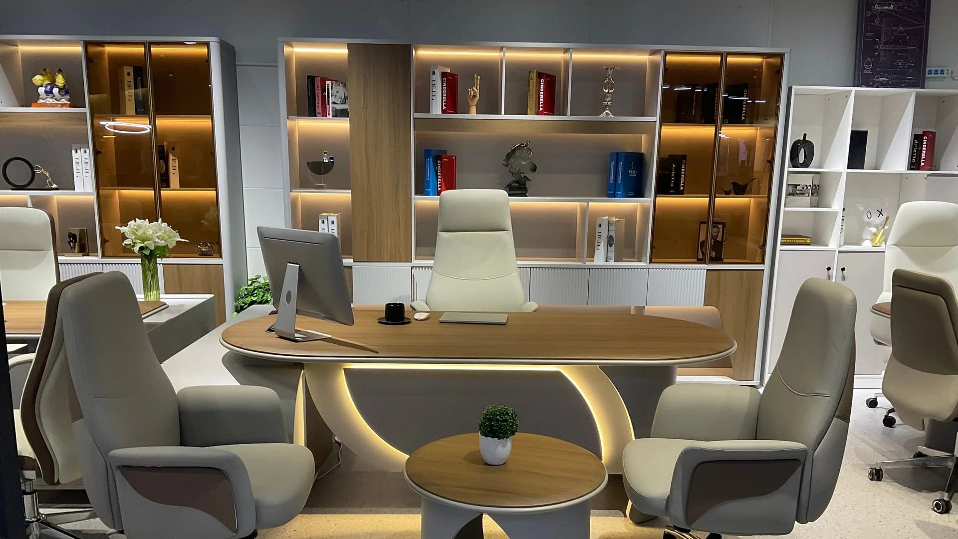 A pale wood desk and cream chairs before lit shelves — Abi Library mood